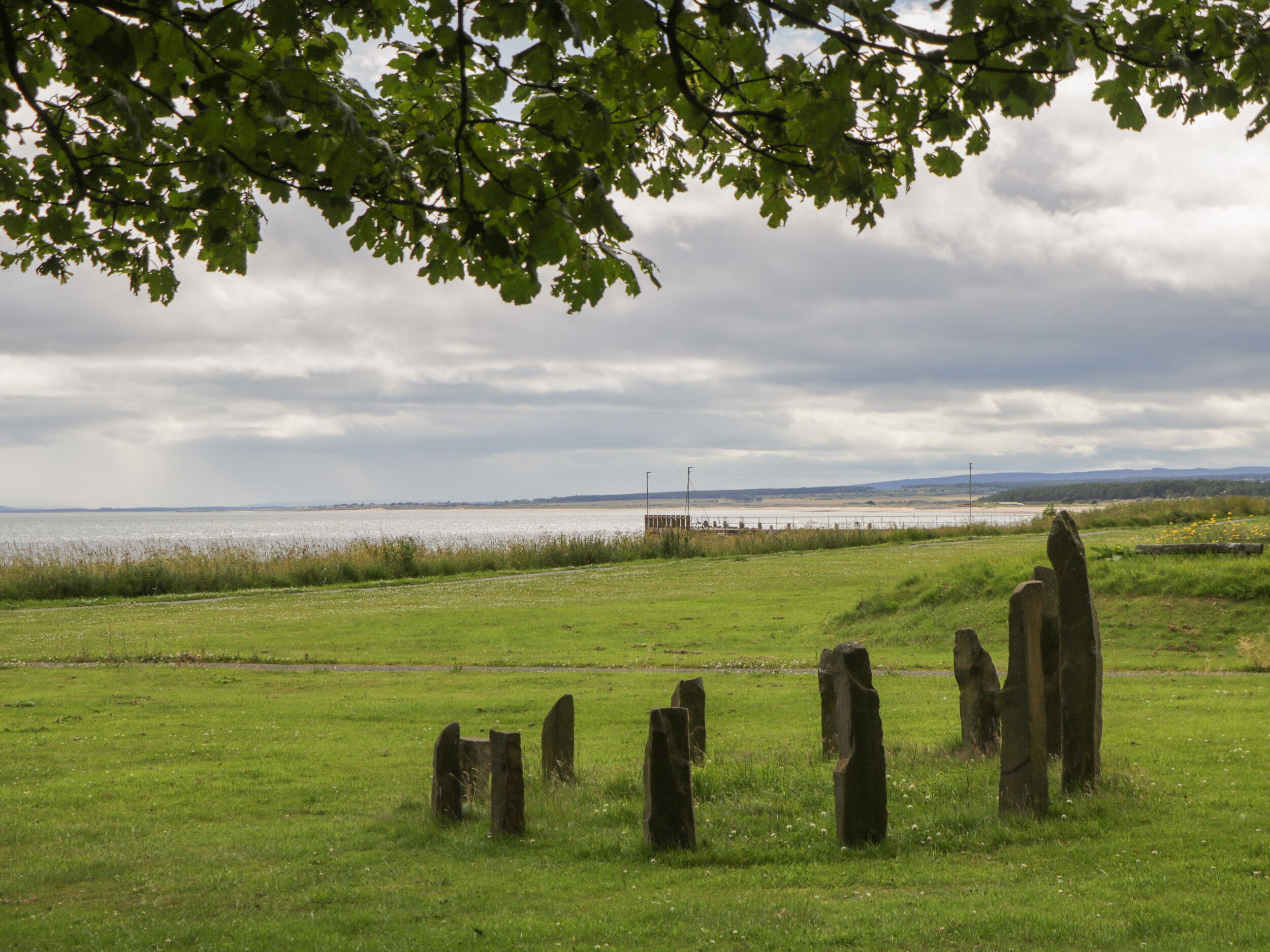 A grassy field with standing stones and a body of water in the background.