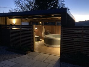 A wooden cabin with a hot tub, a small seating area, and a wooden deck. - The Steading (Rogart)