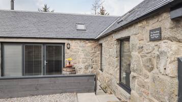 Un edificio de piedra con techo gris, un barril de madera y un letrero que dice "The Steading 48a Blairmore".