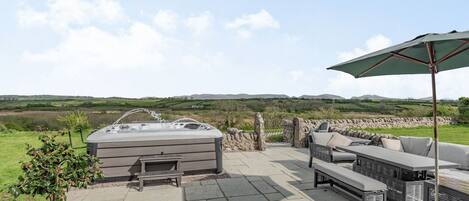 Une terrasse extérieure dotée d’un jacuzzi, d’un espace salon et offrant une vue sur la campagne.