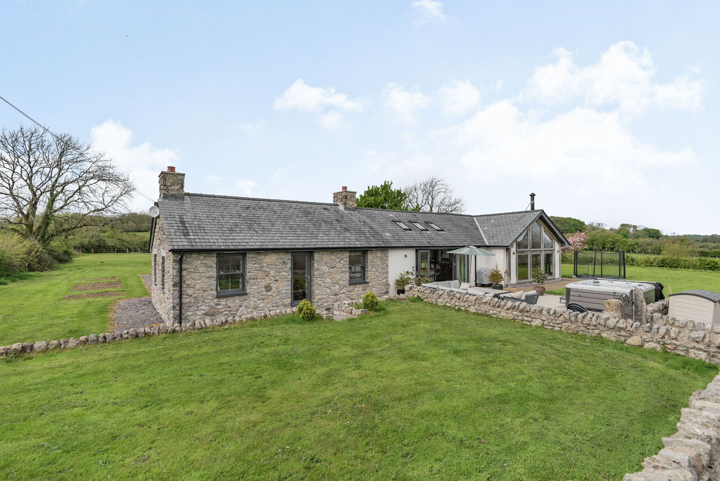 A stone house with a sloped roof, a patio area, and a garden.