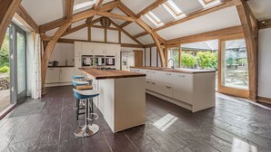 A spacious kitchen with a central island, wooden beams, and large windows.