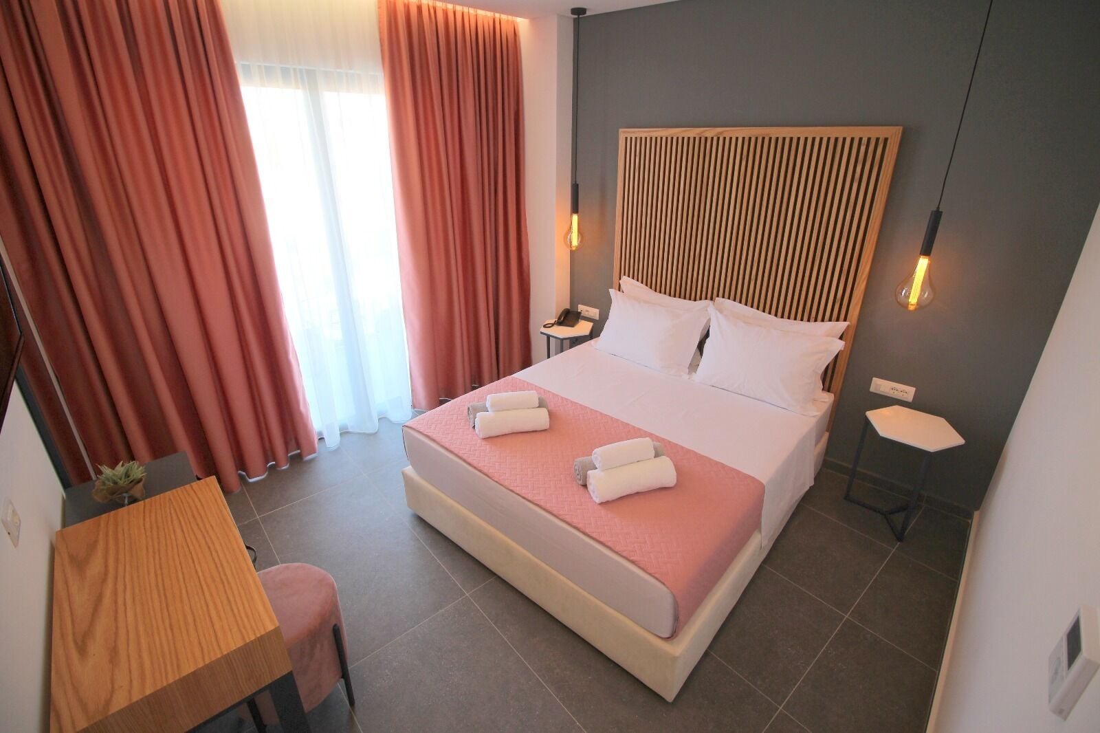 A neatly arranged hotel room with a large bed, a bedside table, a small desk, and a chair.