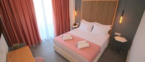 A neatly arranged hotel room with a large bed, a bedside table, a small desk, and a chair.