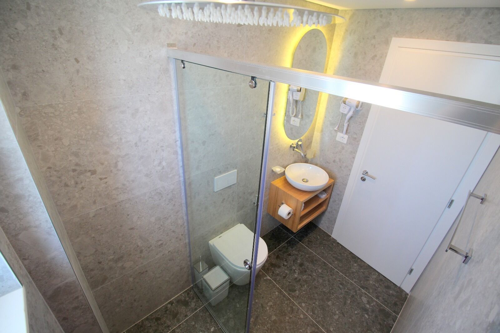 Et moderne badeværelse med en glasafskærmet brusekabine, et hvidt toilet, et trækommode med vask og et spejl.