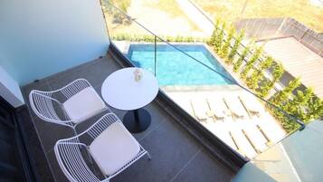 Un balcón con piscina, sillas blancas y una pequeña mesa.