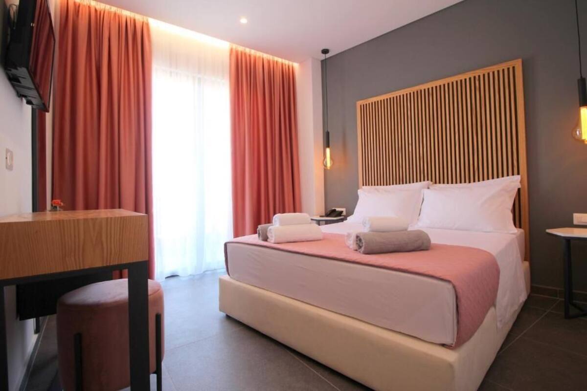 A modern hotel room with a large bed, a wooden headboard, a desk, and a chair.