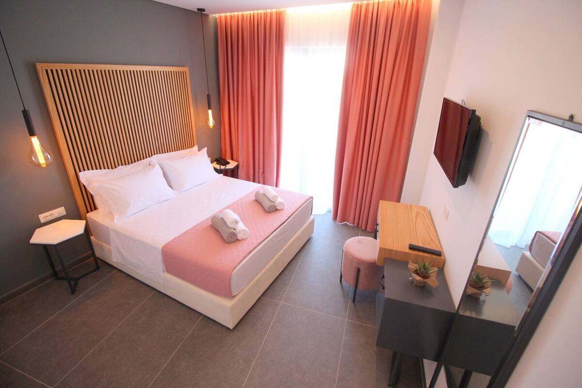 A modern hotel room with a large bed, bedside tables, a desk, a chair, and a mirror.