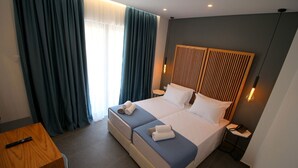 Habitació d'hotel moderna amb un llit gran, dues taules de nit, un panell de llit de fusta i un escriptori amb un comandament a distància.
