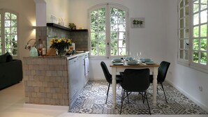 A kitchen with a dining area, featuring a tiled backsplash, a built-in island, and a window with a view of greenery. - Villa Mas du Château - Aircon- Private Pool (Villarzel-Cabardès)