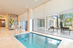 A modern indoor pool area with a glass wall, a lounge chair, and a small table with a plant. - Hiddenbay Teos Hotel Sigacik (Seferihisar)