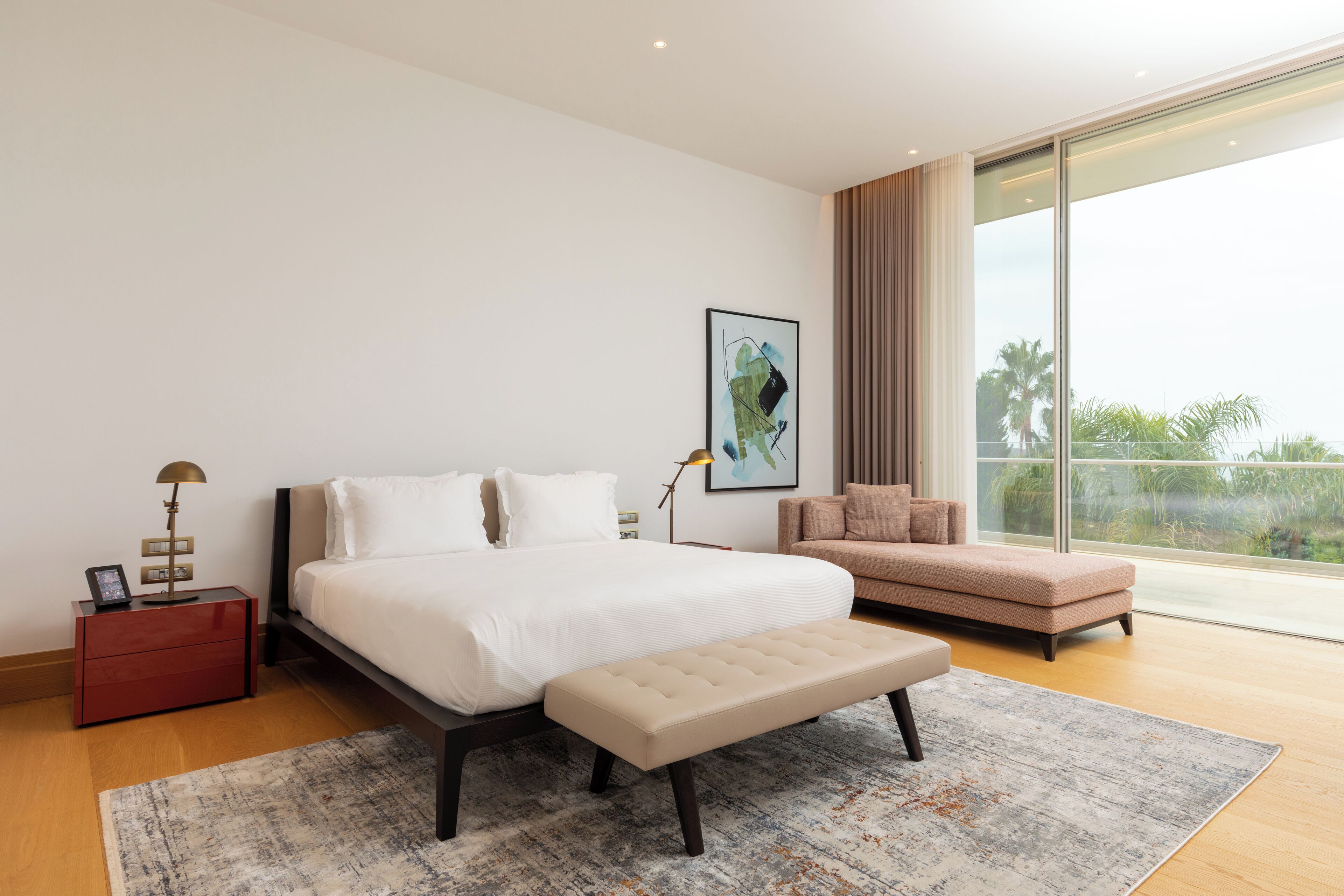 Un dormitorio moderno con una cama grande, un banco, un sofá y un ventanal con vistas.