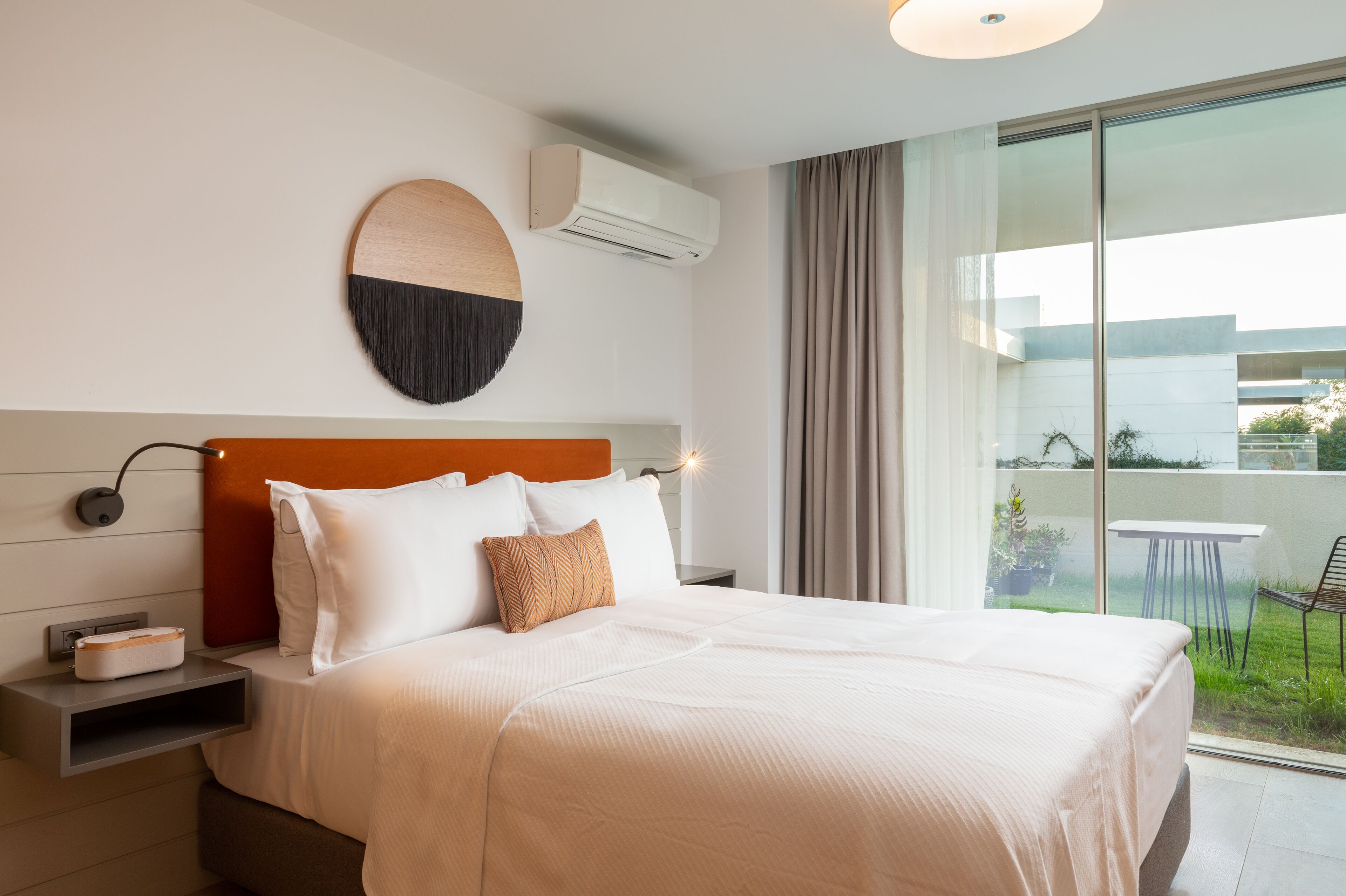 Quarto de hotel moderno com uma cama grande, um detalhe decorativo circular na parede, ar condicionado e vista para o exterior.