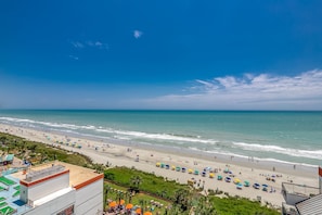 A beach view with a hotel in the foreground, including a pool area and a view of the ocean.