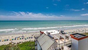 Blick auf den Strand vom Hotel-Dach mit blauem Himmel, Strandstühlen und einer Sandküste.