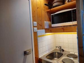 A compact kitchen with a microwave, sink, and wooden cabinets.