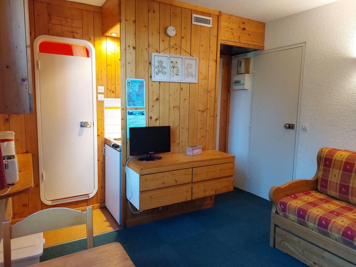 A compact room with wooden walls, a television on a wooden dresser, a sofa, and a door with a red handle.