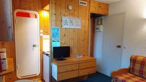 Habitación compacta con paredes de madera, un televisor sobre una cómoda también de madera, un sofá y una puerta con pomo rojo.