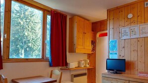Cocina compacta con armarios de madera, una mesa de comedor y un televisor.
