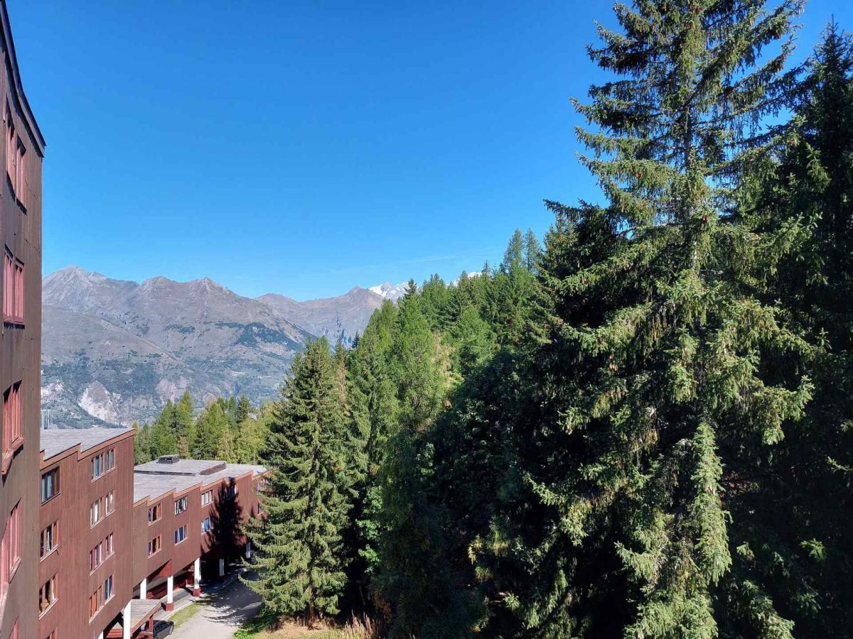 A building with a red facade and multiple windows, surrounded by dense green trees and mountains in the background.