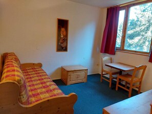 A small, cozy room with a wooden bed, a small table with chairs, and a window with curtains.