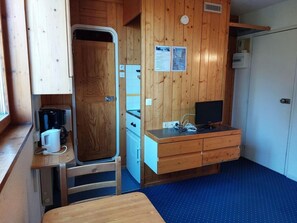 Uma kitchenette compacta com cafeteira, um refrigerador pequeno e uma escrivaninha de madeira com gavetas.