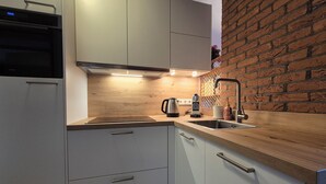 A modern kitchen with white cabinets, a wooden countertop, a stainless steel sink, and a brick wall. - Cozy cottage with fireplace, walking distance from the beach. (Nieuwvliet)