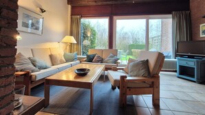 A cozy living room with a sofa, a wooden coffee table, and a TV stand. - Cozy cottage with fireplace, walking distance from the beach. (Nieuwvliet)