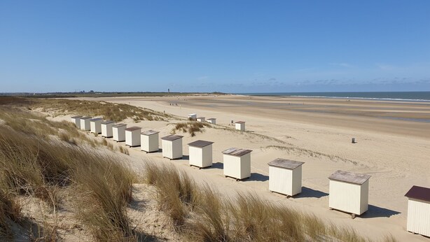A row of white beach huts with a sandy beach and dunes in the background. - Cozy cottage with fireplace, walking distance from the beach. (Nieuwvliet)