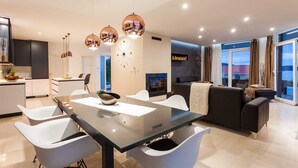 A modern living room with a glass dining table, white chairs, a black sofa, and a fireplace. - Luxury  Villa   Adrian (Vela Luka)