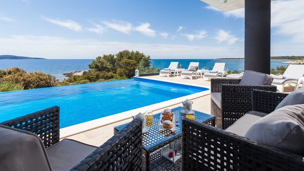 A poolside area with lounge chairs, a table with breakfast items, and a view of the sea. - Luxury  Villa   Adrian (Vela Luka)