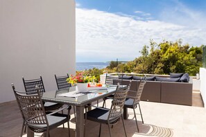 Eine Terrasse mit Glastisch, Korbstühlen, einer Couch und Blick aufs Meer.