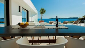 Ein Esstisch mit Blick auf das Meer, eine Weinflasche und eine Obstschale.