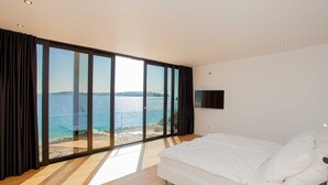 Ein Schlafzimmer mit einer großen Schiebeglastür, die auf einen Balkon mit Meerblick führt.