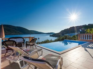 Ein Poolbereich mit Liegestühlen und Blick auf einen See und Hügel.