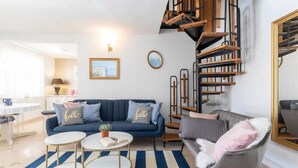 Ein modernes Wohnzimmer mit einem blauen Sofa, zwei runden Tischen, einem Streifen Teppich und einer Treppe mit Holzwangen.