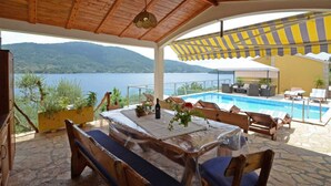 Un espace extérieur aménagé avec des sièges, une piscine, du mobilier en bois et une vue sur le lac et les montagnes.