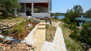 Un bâtiment blanc doté d’un porche abrité, un chemin de pierre menant à l’entrée, et une vue sur un lac.