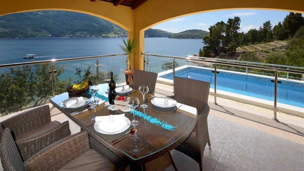 Un coin repas avec une table dressée pour quatre personnes, donnant sur une piscine et un lac.