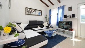 Un salon moderne avec un canapé noir, une table basse en verre et un téléviseur. On y trouve un rideau bleu et une plante sur le rebord de la fenêtre.