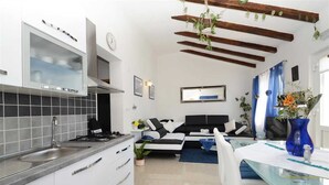 Une cuisine moderne dotée d’une cuisinière intégrée et d’une grande fenêtre. On y trouve un coin repas avec une table et des chaises en verre, ainsi qu’un coin salon avec un canapé et un téléviseur.