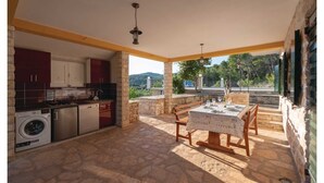 A kitchen with stone flooring, a washing machine, and a dining area with a table set for four. - Holiday House  Gabrijel (Cara)