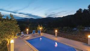 A swimming pool with lounge chairs and lights, surrounded by a fence and trees, with mountains in the background. - Holiday House  Gabrijel (Cara)