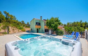 A swimming pool with a hot tub in the foreground, a house with a balcony in the background, and a clear blue sky. - Holiday House  Gabrijel (Cara)
