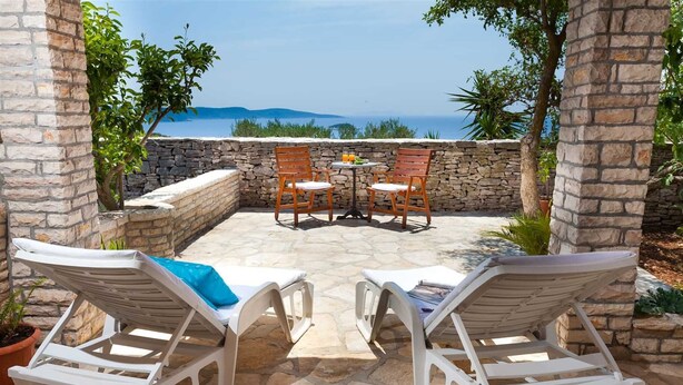 A patio with two white lounge chairs, a small table with chairs, and a stone wall. - House House Čafo- Padovan (Vela Luka)