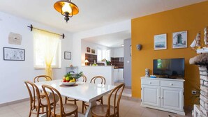 A dining area with a white table and wicker chairs, a fruit bowl, and a yellow wall with artwork. - House House Čafo- Padovan (Vela Luka)