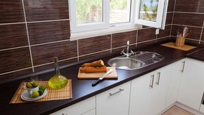 A kitchen with dark brown tiles, a window, a sink, and a cutting board with bread and a knife. - House House Čafo- Padovan (Vela Luka)