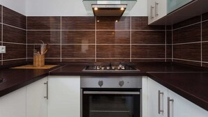 A modern kitchen with dark wooden tiles, stainless steel appliances, and white cabinetry. - House House Čafo- Padovan (Vela Luka)