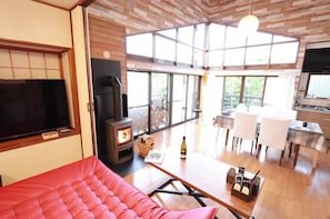 A spacious living area with a large window, a fireplace, a dining table, and a red sofa.