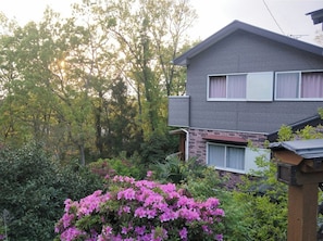 A two-story house with a brick facade, a balcony, and a garden with pink flowers.